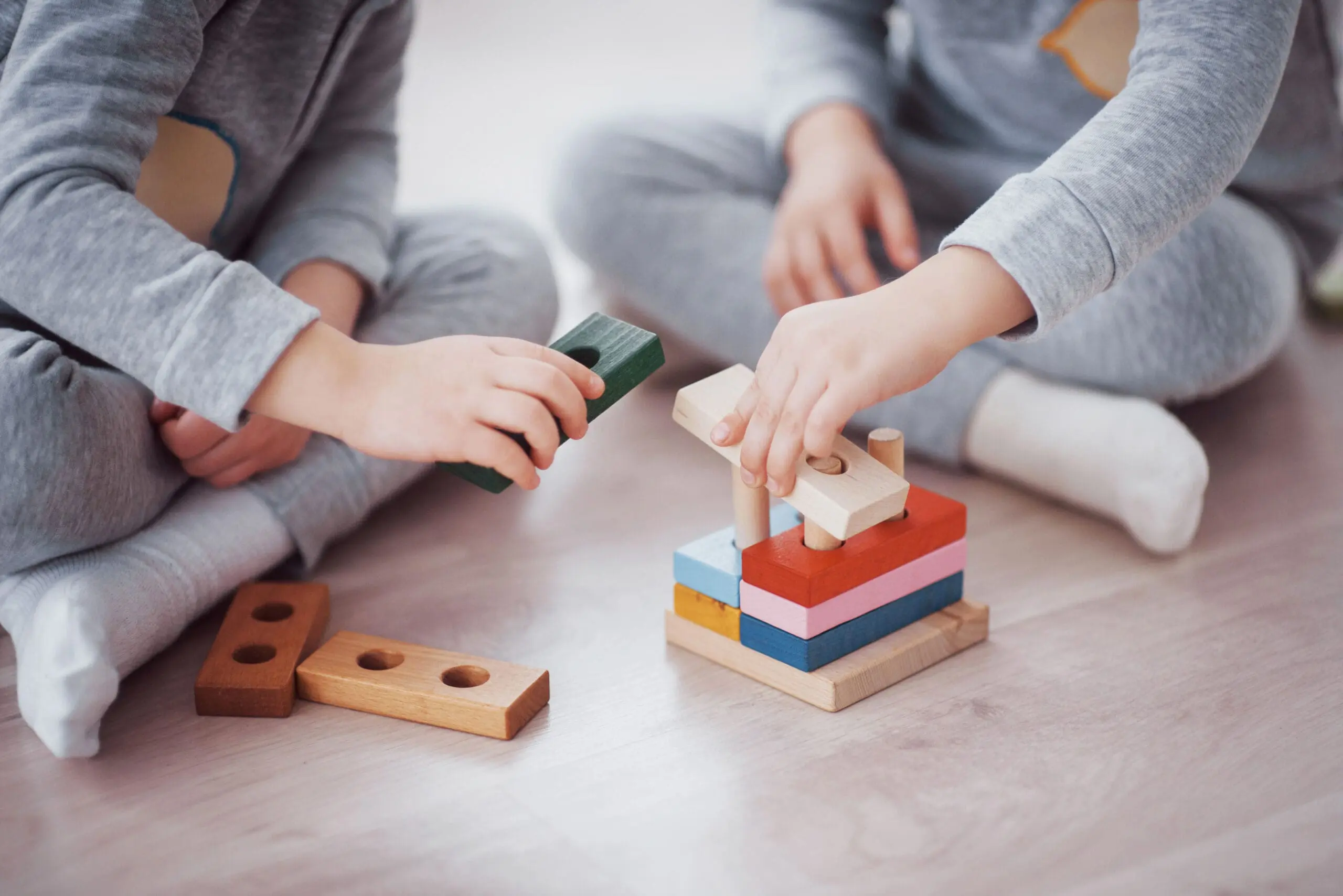 Children play with a toy designer on the floor of the children's room. Two kids playing with colorful blocks. Kindergarten educational games. Close up view.